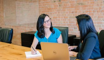 photo of 2 women talking in front of a laptop